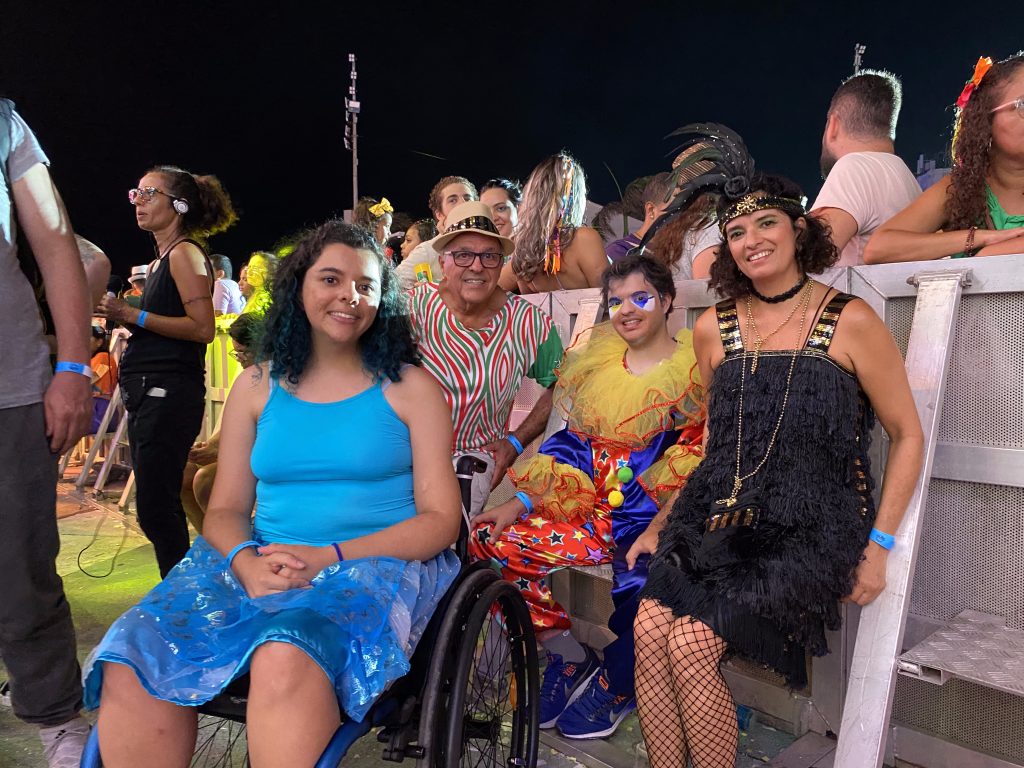 Na fotografica tem quatro pessoas (duas mulheres e dois homens), todos com roupas de carnaval. Estão perto da grade que dividide o palco do Marco Zero e público geral. 