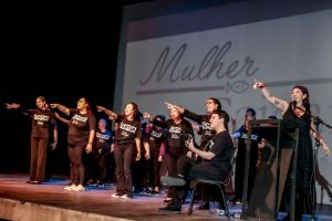 apresentação do grupo de pessoas com sindrome de down e pessoa sem deficiência e todos de preto em cima de um palco,