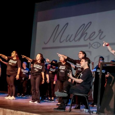 apresentação do grupo de pessoas com sindrome de down e pessoa sem deficiência e todos de preto em cima de um palco,