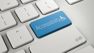 Fotografia de teclado de computador branco, com uma tecla azul em destaque, que está escrita "Acessibilidade" e, ao lado, um símbolo da pessoa com deficiência física.