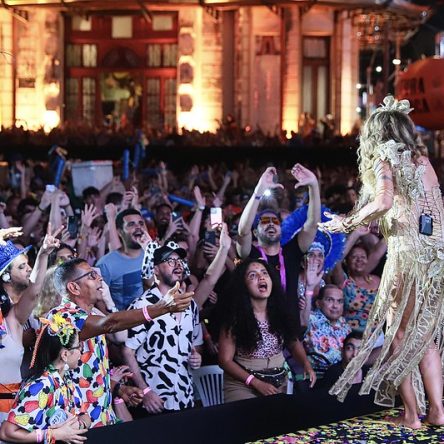 Fotografia de uma plateia de pessoas com deficiência voltada para o palco onde Elba Ramalho se apresenta, com um vestido dourado.