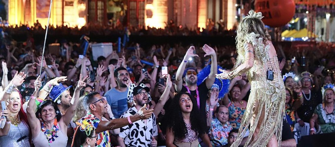 Fotografia de uma plateia de pessoas com deficiência voltada para o palco onde Elba Ramalho se apresenta, com um vestido dourado.